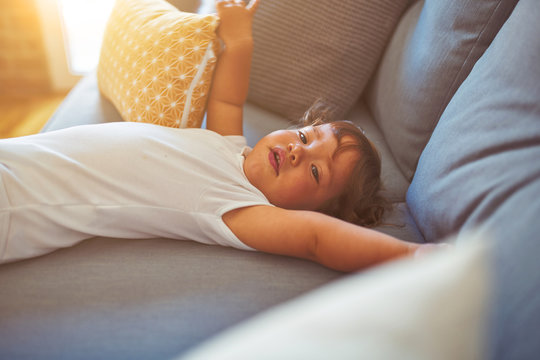 Beautiful toddler child girl wearing white bodysuit lying down on the sofa