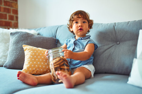 Beautiful toddler child girl holding jar of cookies sitting on the sofa