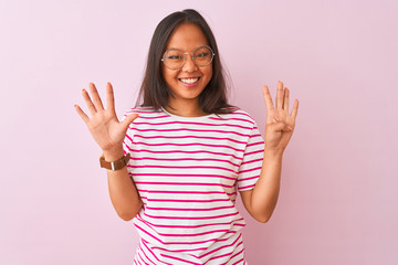 Young chinese woman wearing striped t-shirt and glasses over isolated pink background showing and pointing up with fingers number nine while smiling confident and happy.