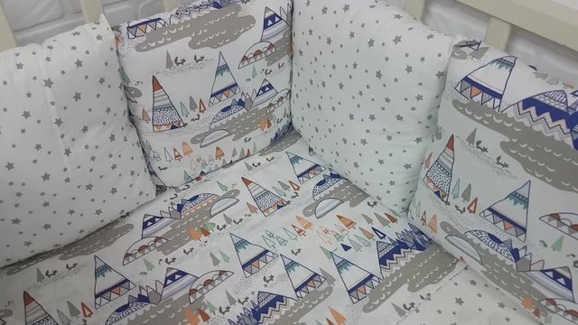 Children's bed linen with a pattern of stars and teepees. Pillows, blankets, sheets in the baby's cot.