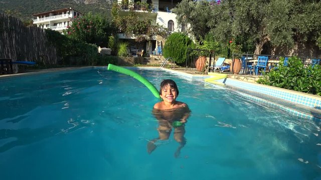 Kas, Turkey - 28th of September 2019: 4K Kid having fun with a nooddle in the countryside swimming pool