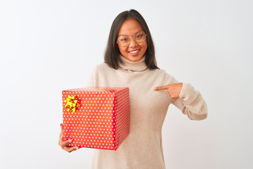 Young chinese woman wearing glasses holding birthday gift over isolated white background with surprise face pointing finger to himself