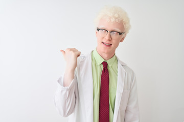 Young albino blond scientist man wearing coat and glasses over isolated white background smiling with happy face looking and pointing to the side with thumb up.