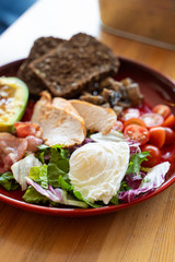 Substantial hotel breakfast with avocado and nuts, rye toasts, vegetables, fried bacon, chicken and poached egg