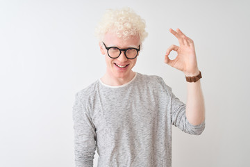 Young albino blond man wearing striped t-shirt and glasses over isolated white background smiling positive doing ok sign with hand and fingers. Successful expression.