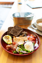 Substantial breakfast with avocado and nuts, rye toasts, vegetables, fried bacon, chicken and poached egg