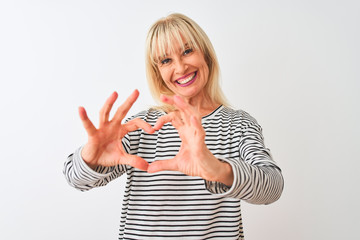 Middle age woman wearing navy striped t-shirt standing over isolated white background smiling in love showing heart symbol and shape with hands. Romantic concept.
