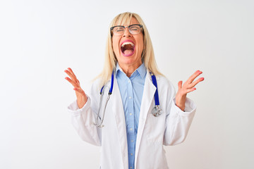 Middle age doctor woman wearing glasses and stethoscope over isolated white background celebrating mad and crazy for success with arms raised and closed eyes screaming excited. Winner concept