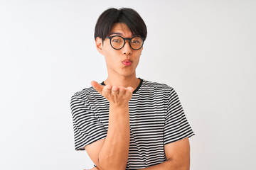 Chinese man wearing glasses and navy striped t-shirt standing over isolated white background looking at the camera blowing a kiss with hand on air being lovely and sexy. Love expression.