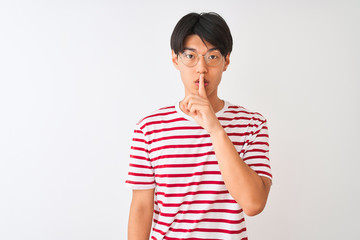 Young chinese man wearing glasses and striped t-shirt standing over isolated white background asking to be quiet with finger on lips. Silence and secret concept.