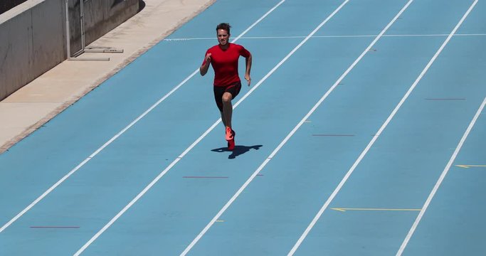Sprinter runner athlete man sprinting training on outdoor athletics track and field running lanes at stadium. Sport and health active lifestyle on college. SLOW MOTION 59.94 FPS.