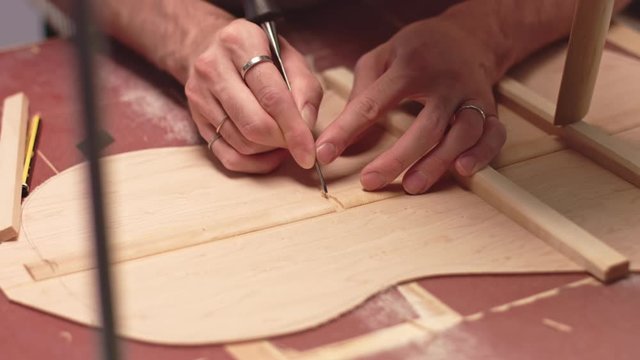 Guitar maker cuts braces to insert horizontal braces in acoustic guitar soundboard, close up
