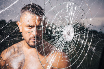 macho man glasscutter behind crushed glass. sexy hispanic man broken mirror. bullet hole in glass....