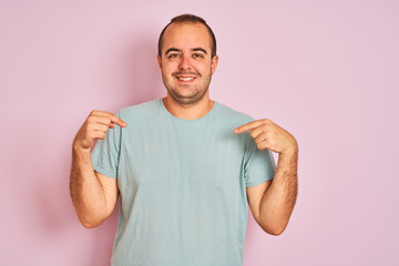 Fototapeta premium Young man wearing blue casual t-shirt standing over isolated pink background looking confident with smile on face, pointing oneself with fingers proud and happy.
