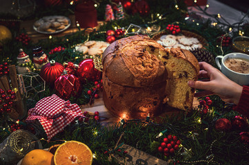 Young woman holding a slice of panettone at Christmas and in the background a table with holiday...