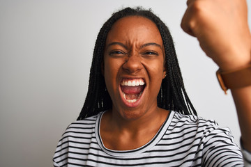 Young african american woman wearing striped t-shirt standing over isolated white background annoyed and frustrated shouting with anger, crazy and yelling with raised hand, anger concept