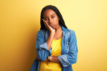 Young african american woman wearing denim shirt standing over isolated yellow background thinking looking tired and bored with depression problems with crossed arms.