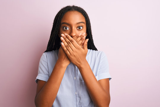 Young african american woman wearing striped shirt standing over isolated pink background shocked covering mouth with hands for mistake. Secret concept.