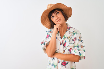 Beautiful woman on vacation wearing summer shirt and hat over isolated white background with hand on chin thinking about question, pensive expression. Smiling with thoughtful face. Doubt concept.