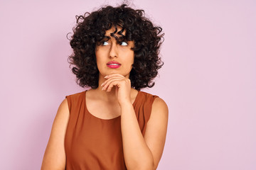 Fototapeta premium Young arab woman with curly hair wearing t-shirt over isolated pink background serious face thinking about question, very confused idea