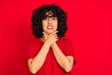 Young arab woman with curly hair wearing casual t-shirt over isolated red background shouting and suffocate because painful strangle. Health problem. Asphyxiate and suicide concept.