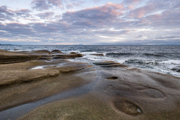 rocky coast line filled with sand stone by the ocean under cloudy sky with a hint of pink colour near dawn 