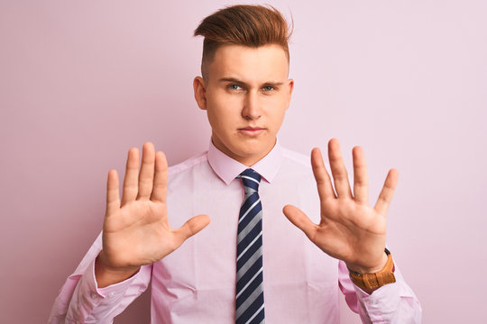 Young handsome businessman wearing shirt and tie standing over isolated pink background Moving away hands palms showing refusal and denial with afraid and disgusting expression. Stop and forbidden.