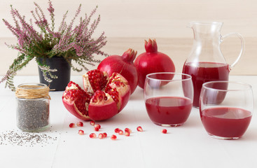 2 glasses of fresh pomegranate juice with few ripe real pomegranates on dark blue background. Partially peeled pomegranate, rouge seeds and peeling knife in foreground.