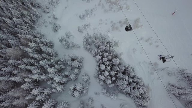 Top down wide angle aerial shot of two skiers offside the slope. Two passing ski gondolas gives the footage a graphic look.