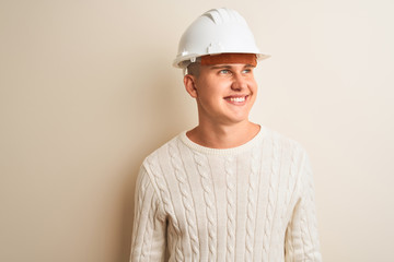 Handsome architect man wearing security helmet standing over isolated white background looking away to side with smile on face, natural expression. Laughing confident.