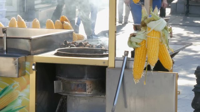 Fresh corn on the street kiosk counter. Street food, seller sells boiled corn in row to customers on a city street. Healthy Food and Products Concept, Passersby pass by