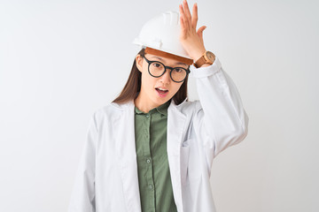 Young chinese engineer woman wearing coat helmet glasses over isolated white background surprised...
