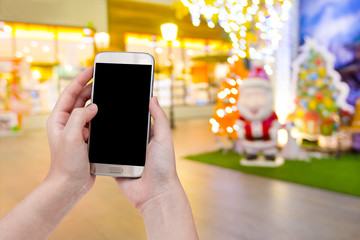 hand holding mobile smart phone with santa claus doll christmas blur background