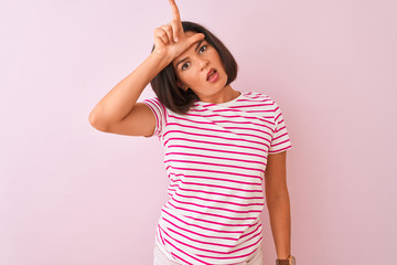 Young beautiful woman wearing striped t-shirt standing over isolated pink background making fun of...