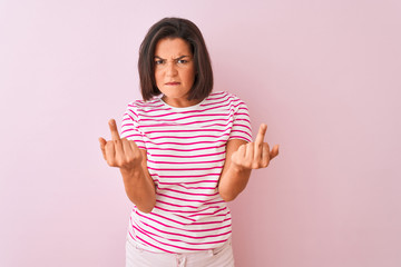 Young beautiful woman wearing striped t-shirt standing over isolated pink background Showing middle finger doing fuck you bad expression, provocation and rude attitude. Screaming excited