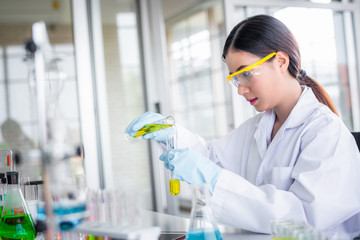 Attractive scientist woman looking chemical sample in flask at laboratory with lab glassware background. Science or chemistry research and development concept.