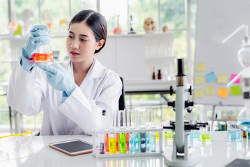 Attractive scientist woman looking chemical sample in flask at laboratory with lab glassware...