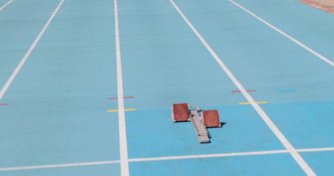 Sprinter runner athlete running in starting blocks training sprinting start of sprint on blue running tracks at outdoor athletics track and field stadium. Sport and fitness man running sprinting.