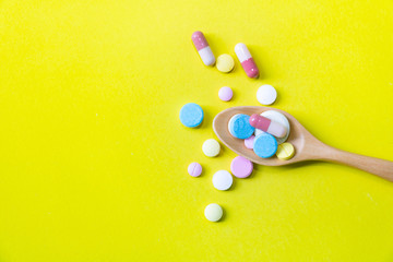 Top view Medicine on wood spoon.Assorted pharmaceutical red capsules with Multi color vitamins and supplements.They are on Yellow background and copy space.Photo concept healthy and medication.