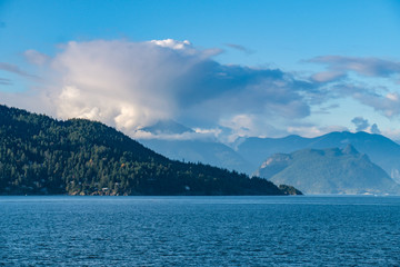 dense cloud with beautiful shape above the mountains of forest covered islands by the blue ocean on a sunny afternoon