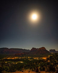Moon rising at Airport Mesa vortex over Sedona city lights at night with red sandstone buttes