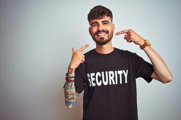 Young safeguard man with tattoo wering security uniform over isolated white background smiling...