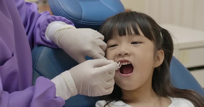 Dentist in an uniform and latex gloves cleans little girl patient's teeth with dental floss in a dental clinic. Dental hygienist teach little girl how to use oral floss for teeth brushing. 