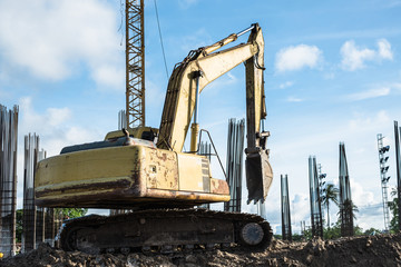 Fototapeta na wymiar Old yellow backhoe or excavator work digging soil at new building construction site with steel concrete pillars in the back.