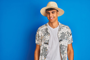 Indian man on vacation wearing hawiaian shirt summer hat over isolated blue background looking away to side with smile on face, natural expression. Laughing confident.