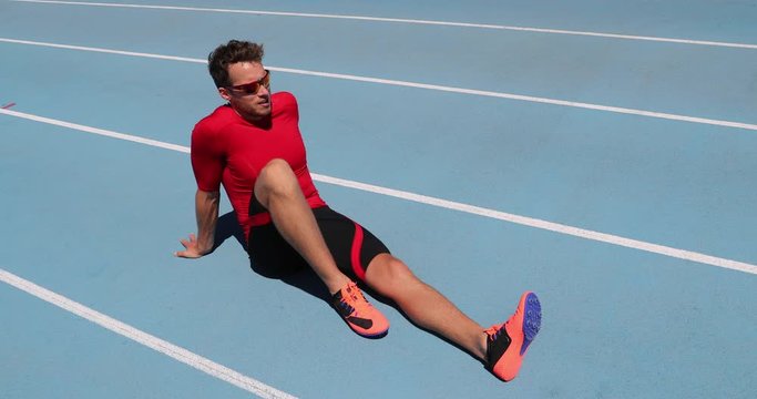 Athlete sprinter relaxing after run on athletics running track and field stadium. Male runner wearing spike running shoes. Man track runner relaxing after training outdoors. Fitness and sports.