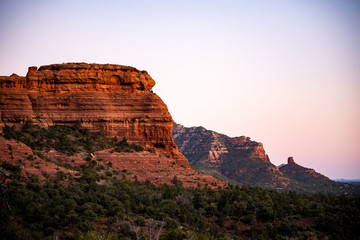 Fototapeta na wymiar Row of red sandstone formations Capitol Butte glowing at sunset in Sedona, AZ with Coffee Pot Rock in distance