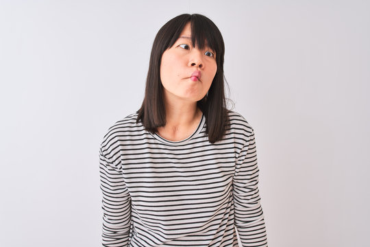 Young beautiful chinese woman wearing black striped t-shirt over isolated white background making fish face with lips, crazy and comical gesture. Funny expression.