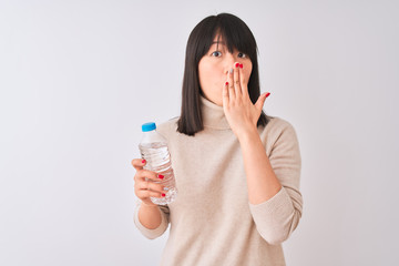 Young beautiful Chinese woman holding bottle of water over isolated white background cover mouth with hand shocked with shame for mistake, expression of fear, scared in silence, secret concept