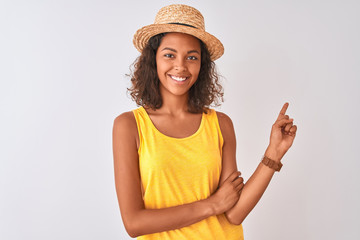 Obraz na płótnie Canvas Young brazilian woman wearing yellow t-shirt and summer hat over isolated white background with a big smile on face, pointing with hand and finger to the side looking at the camera.